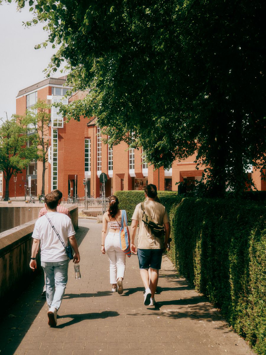 Students walking towards a university building on a tree-lined campus